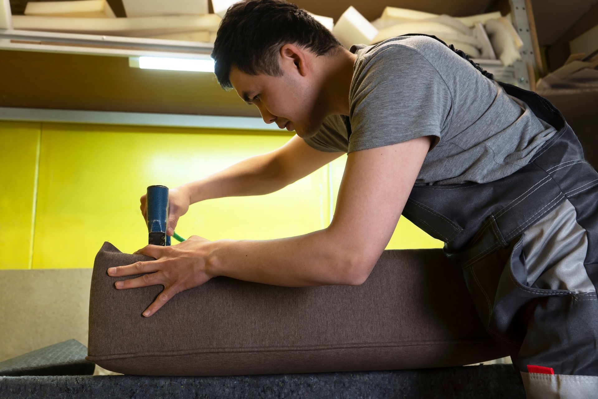 Furniture upholstery. A carpenter fixes the fabric with a pneumatic stapler.